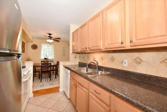 Kitchen featuring white appliances, light brown cabinetry, dark countertops, light tile patterned floors, and backsplash | Image 17