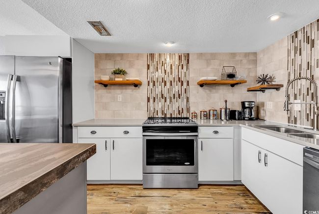 Kitchen with light wood finished floors, a sink, appliances with stainless steel finishes, and open shelves | Image 20