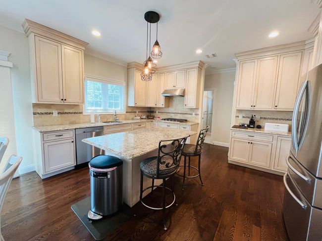 Kitchen with stainless steel appliances, under cabinet range hood, ornamental molding, decorative backsplash, and a breakfast bar area | Image 6