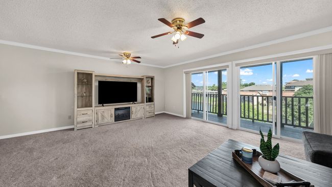 living room with ceiling fan, light carpet, a textured ceiling, and ornamental molding | Image 6