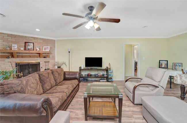 Living room featuring light wood-type flooring, ornamental molding, a ceiling fan, baseboards, and a fireplace | Image 11