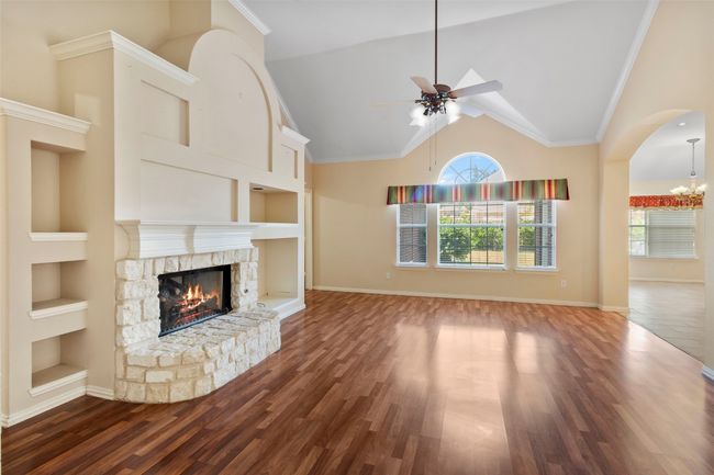 Unfurnished living room with built in shelves, ceiling fan, a fireplace, high vaulted ceiling, and wood finished floors | Image 19