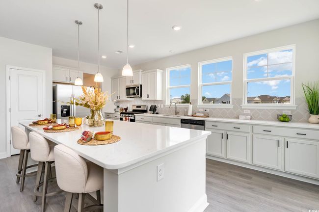 Kitchen with stainless steel appliances, a kitchen breakfast bar, light wood-style floors, a center island, and decorative backsplash | Image 6