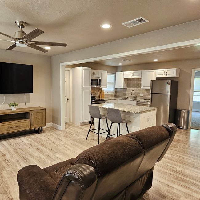 Open concept living area with light wood-style floors, a ceiling fan, baseboards, recessed lighting, and a textured ceiling. | Image 4