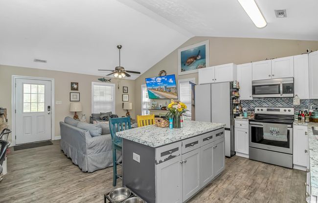 Kitchen featuring appliances with stainless steel finishes, light wood finished floors, a center island, open floor plan, and ceiling fan | Image 10