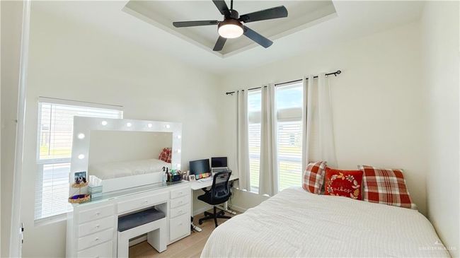 Bedroom featuring a tray ceiling, light wood finished floors, an office area, and a ceiling fan | Image 7