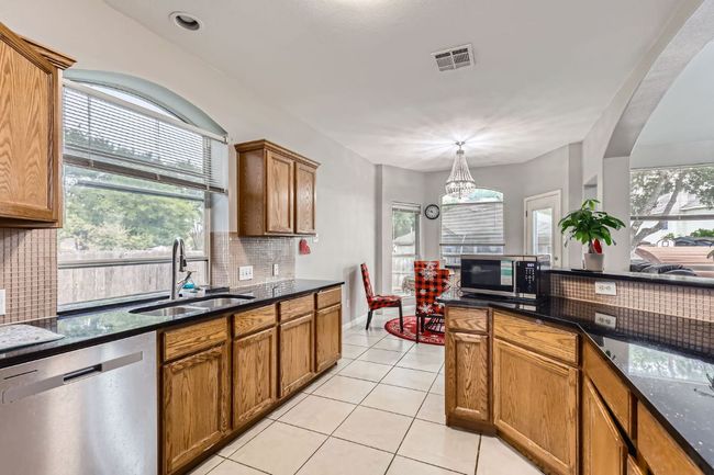 Kitchen featuring stainless steel appliances, decorative backsplash, brown cabinets, and light tile patterned flooring | Image 11