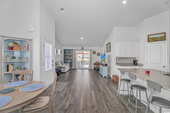 Kitchen with lofted ceiling, a breakfast bar, white cabinetry, dark hardwood / wood-style floors, and light stone counters | Image 7