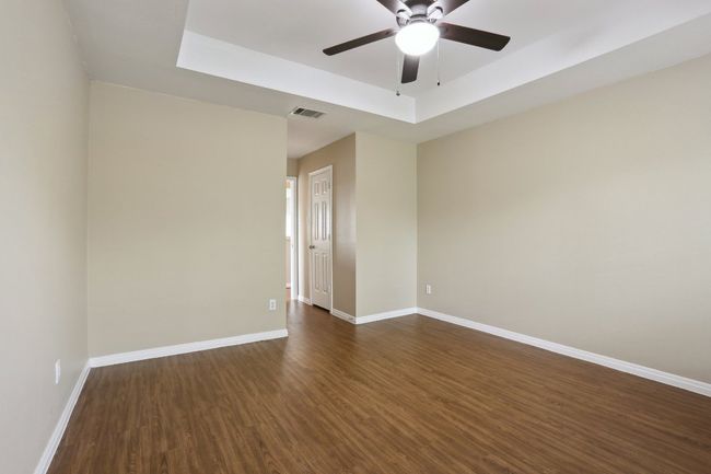 Unfurnished room with dark wood finished floors, baseboards, visible vents, a ceiling fan, and a tray ceiling | Image 26