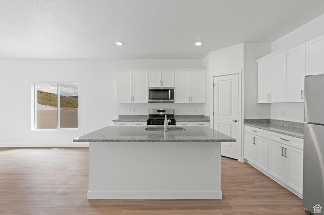 Kitchen with recessed lighting, a center island with sink, stainless steel appliances, and white cabinetry | Image 4