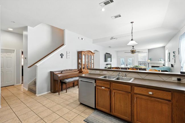 Kitchen featuring brown cabinetry, dishwasher, a tiled fireplace, a ceiling fan, and dark countertops | Image 4