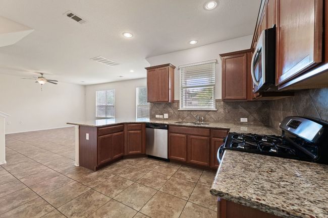 Kitchen featuring appliances with stainless steel finishes, a peninsula, tasteful backsplash, light tile patterned flooring, and recessed lighting | Image 8