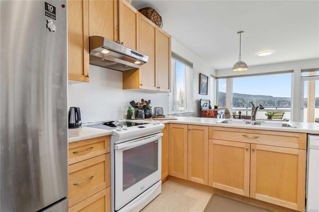 Kitchen with light brown cabinetry, white appliances, light countertops, under cabinet range hood, and a sink | Image 12