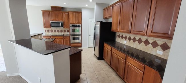 Kitchen with brown cabinets, light tile patterned floors, decorative backsplash, dark stone counters, and stainless steel appliances | Image 9