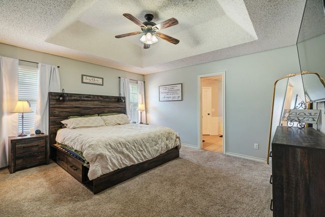 Bedroom featuring light carpet, a textured ceiling, a raised ceiling, a ceiling fan, and ensuite bath | Image 9