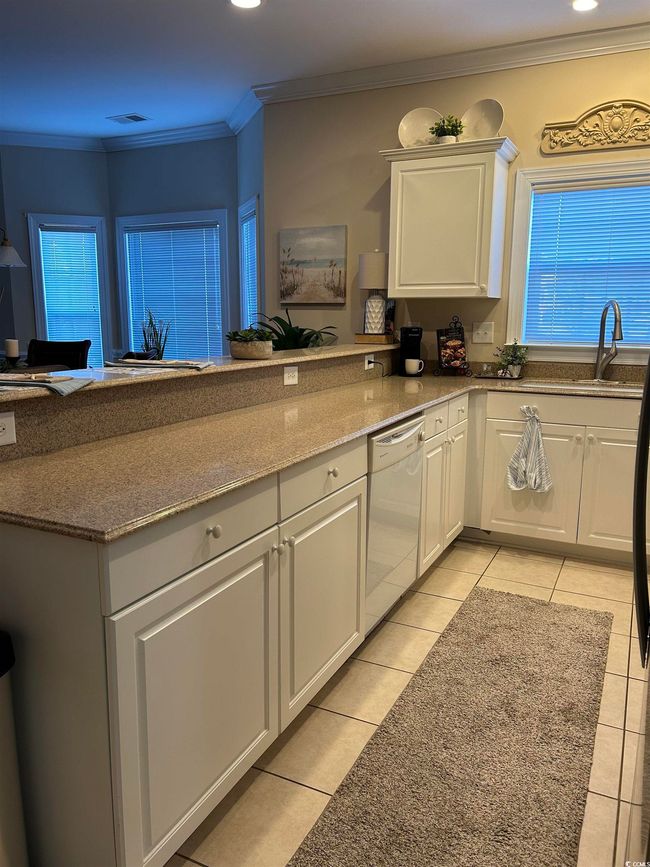 Kitchen featuring white dishwasher, a sink, white cabinetry, ornamental molding, and dark stone counters | Image 4