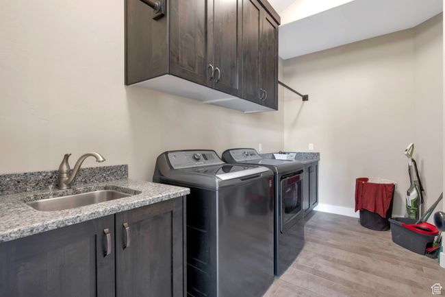 Clothes washing area with baseboards, light wood-type flooring, a sink, cabinet space, and washing machine and clothes dryer | Image 20