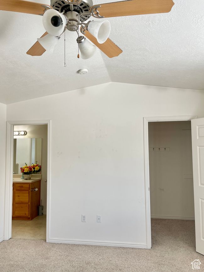 Unfurnished bedroom featuring a spacious closet, light carpet, vaulted ceiling, ensuite bathroom, and ceiling fan | Image 18