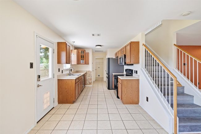Kitchen featuring stainless steel appliances, brown cabinetry, light tile patterned flooring, and light countertops | Image 4
