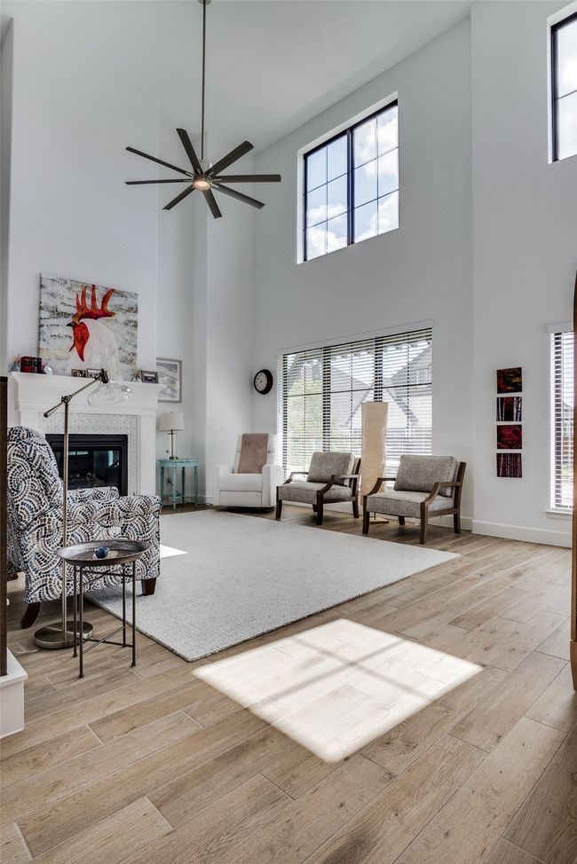 Living room with a towering ceiling, wood finished floors, a ceiling fan, and a fireplace | Image 4