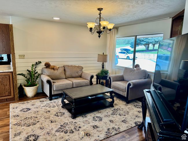 Living room with wood finished floors, a chandelier, a wainscoted wall, and a textured ceiling | Image 9