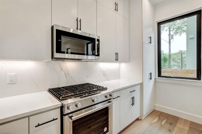 Kitchen featuring stainless steel appliances, backsplash, light wood-style flooring, light countertops, and white cabinetry | Image 12