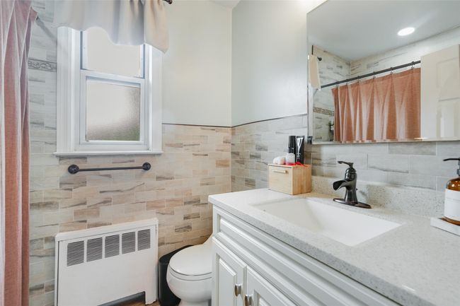 Bathroom with radiator, vanity, tile walls, toilet, and a shower with curtain | Image 11