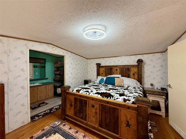 Bedroom with lofted ceiling, ornamental molding, a textured ceiling, wood finished floors, and wallpapered walls | Image 15