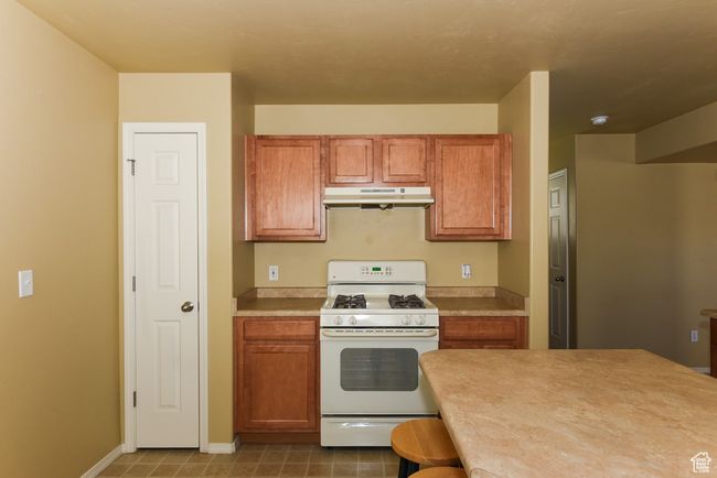 Kitchen with light countertops, white gas range oven, under cabinet range hood, and brown cabinets | Image 14