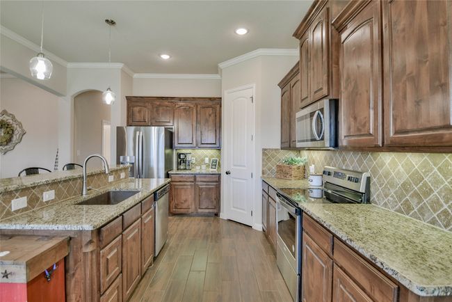 Kitchen featuring dark wood-type flooring, appliances with stainless steel finishes, a sink, a center island with sink, and decorative backsplash | Image 14