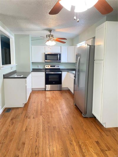 Kitchen featuring light hardwood / wood-style floors, appliances with stainless steel finishes, a textured ceiling, and white cabinets | Image 3