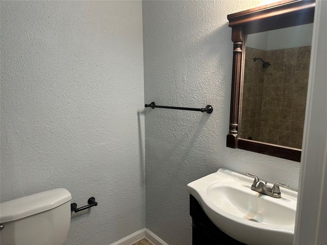 Bathroom featuring a textured wall, toilet, a shower, and a sink | Image 13