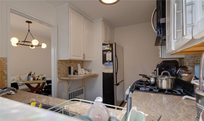 Kitchen featuring freestanding refrigerator, backsplash, white cabinets, and light stone countertops | Image 5