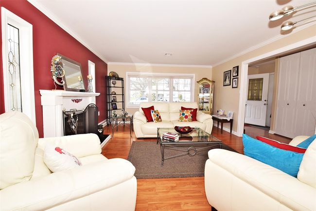 Living room featuring a wood-burning fireplace with raised hearth, wood finished floors, and crown molding | Image 4