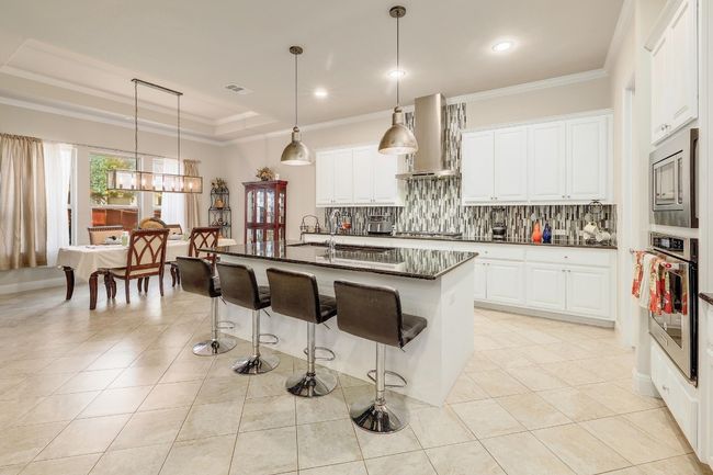 Kitchen with ornamental molding, backsplash, a breakfast bar area, light tile patterned floors, and extractor fan | Image 10