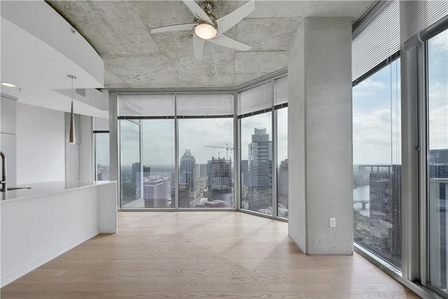 Empty room with a city view, expansive windows, wood finished floors, and ceiling fan | Image 11