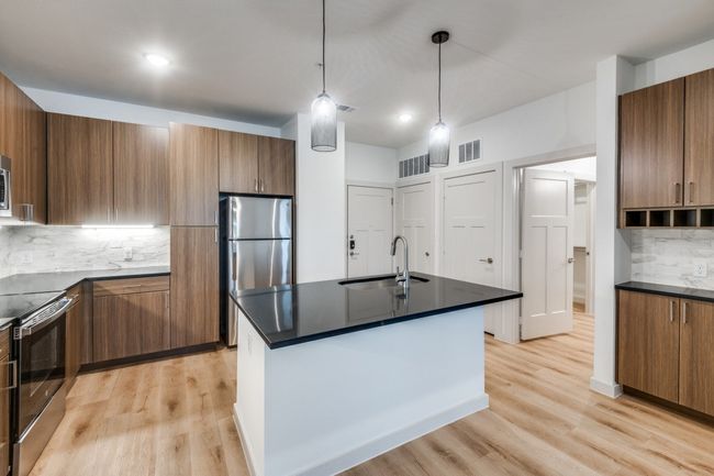 Kitchen with light wood-style flooring, a sink, dark countertops, stainless steel appliances, and brown cabinetry | Image 13