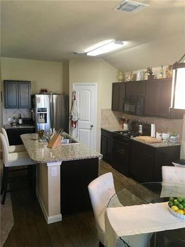 Kitchen featuring black appliances, dark wood-style flooring, an island with sink, lofted ceiling, and light stone countertops | Image 4