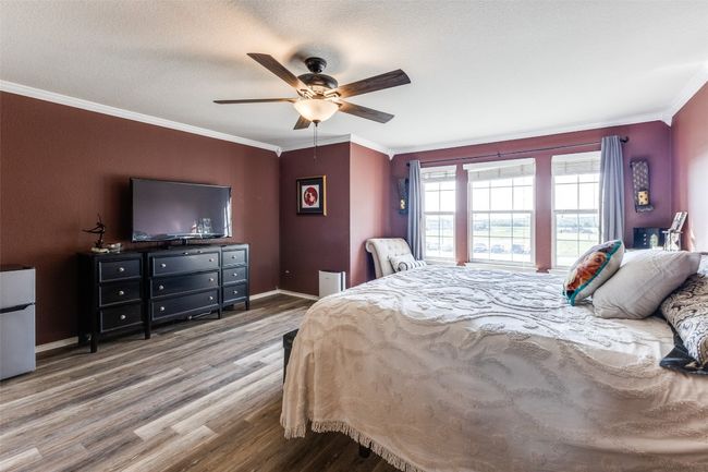 Bedroom with wood finished floors, crown molding, freestanding refrigerator, a ceiling fan, and baseboards | Image 30