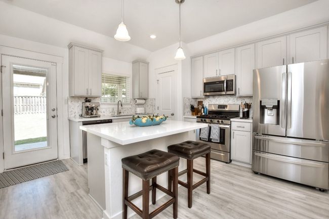 Kitchen with tasteful backsplash, light countertops, light wood-type flooring, appliances with stainless steel finishes, and a breakfast bar area | Image 13