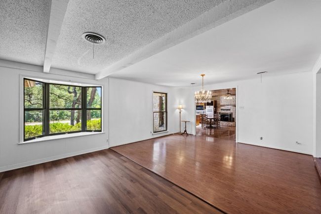 Unfurnished living room with a chandelier, wood & LVP finished floors, baseboards, and beamed ceiling | Image 9