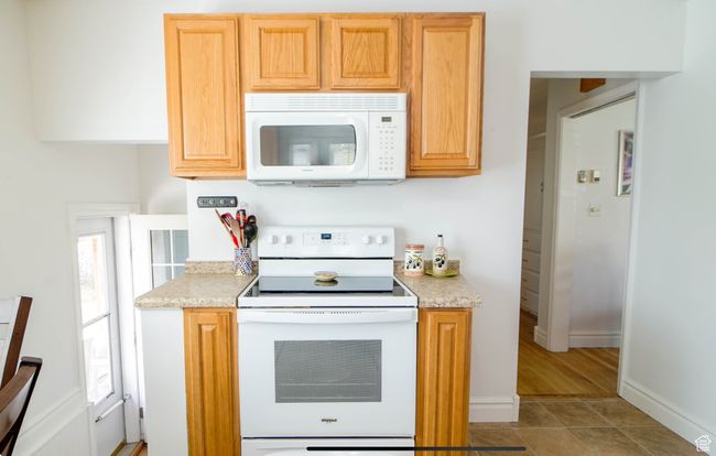 Kitchen with white appliances, light countertops, baseboards, and light tile patterned floors | Image 7