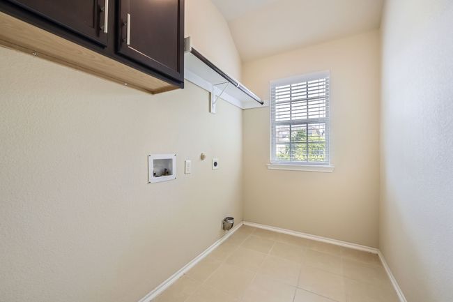 Laundry area featuring hookup for an electric dryer, cabinet space, washer hookup, light tile patterned flooring, and hookup for a gas dryer | Image 26