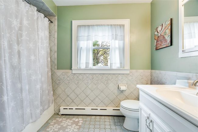 Full bathroom featuring a baseboard heating unit, tile walls, vanity, and toilet | Image 25