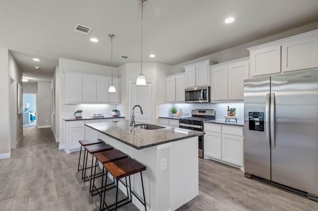 Kitchen with stainless steel appliances, backsplash, a breakfast bar, a center island with sink, and dark stone countertops | Image 4