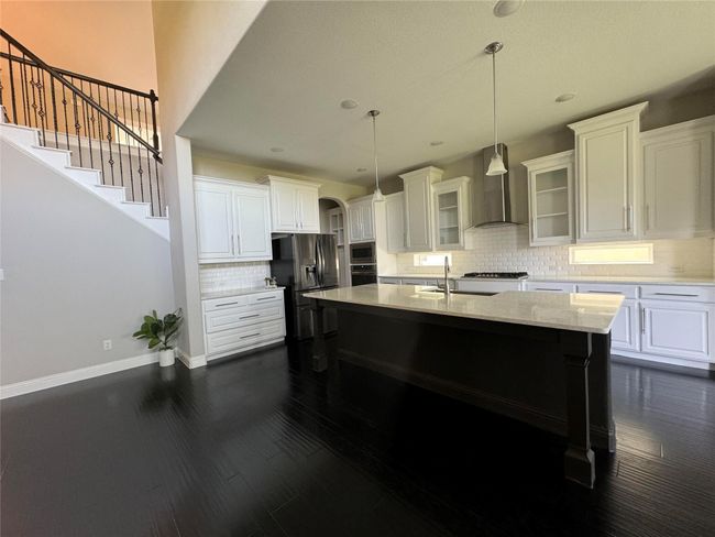 Kitchen with wall chimney exhaust hood, appliances with stainless steel finishes, white cabinets, tasteful backsplash, and glass insert cabinets | Image 7
