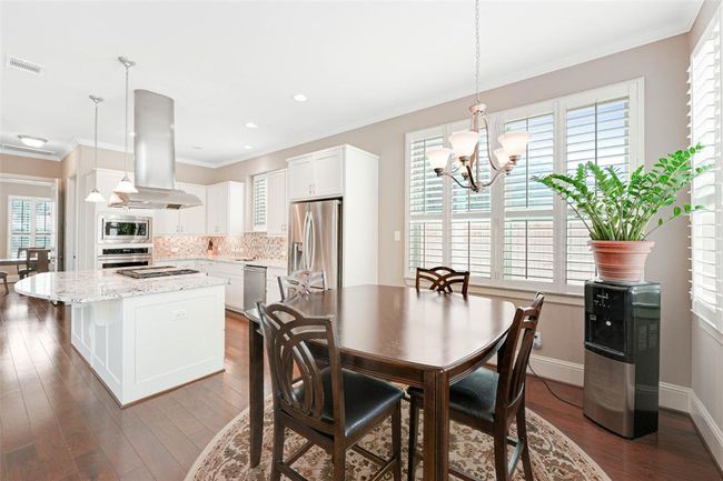 Sunlit breakfast area with large windows and plantation shutters, adjacent to a spacious kitchen featuring granite counters, stainless steel appliances, and an oversized island with bar seating—perfect for casual dining and morning coffee. | Image 16