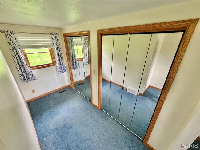 Unfurnished bedroom with carpet flooring, two closets, baseboards, and a textured ceiling | Image 15