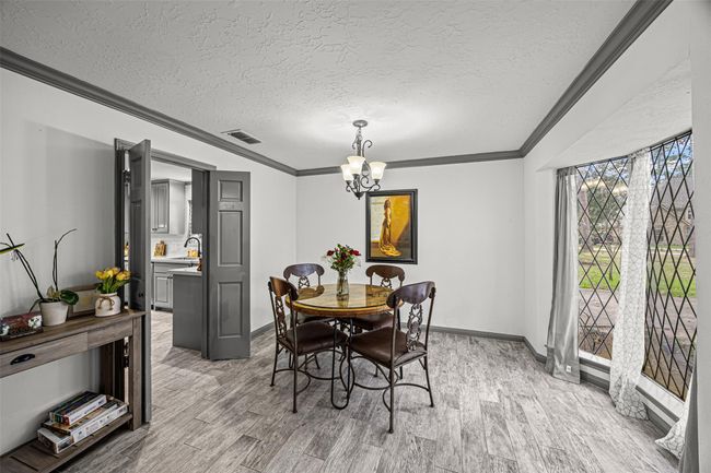 This dining area features a cozy round table with elegant chairs, set beneath a modern chandelier. The room is bright, with large windows providing a view of the garden. The space connects to the kitchen through a doorway, and the neutral tones and tasteful decor create a welcoming atmosphere. | Image 16