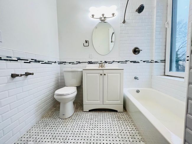 Bathroom is fully tiled and has a large window. | Image 11